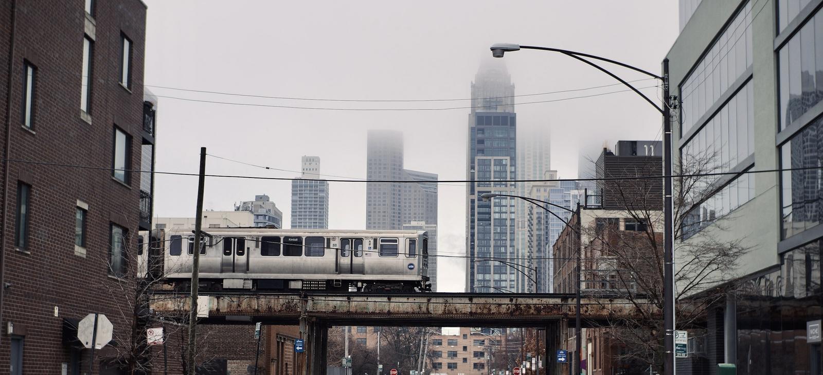 A CTA train crossing a neighborhood street in Chicago, the skyline in fog behind it.