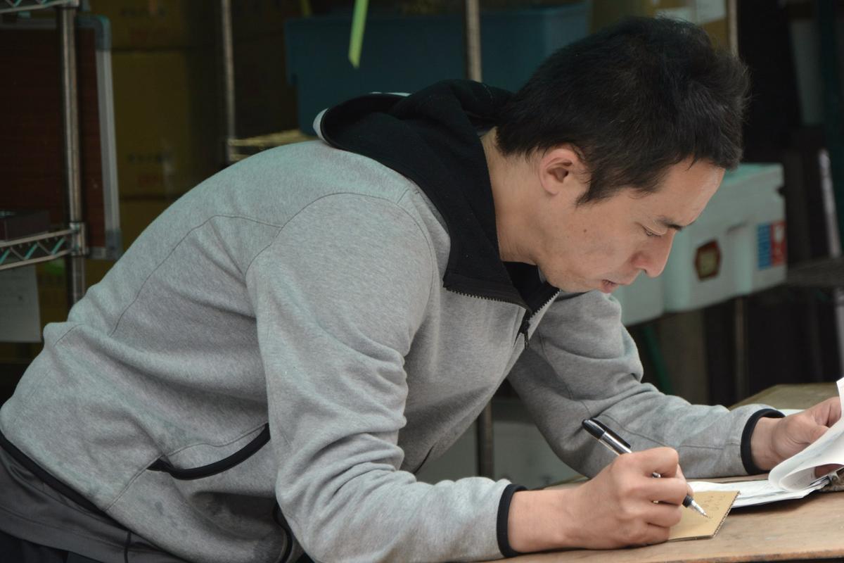 A man leaning over a workbench in a stockroom, filling in paperwork by hand.