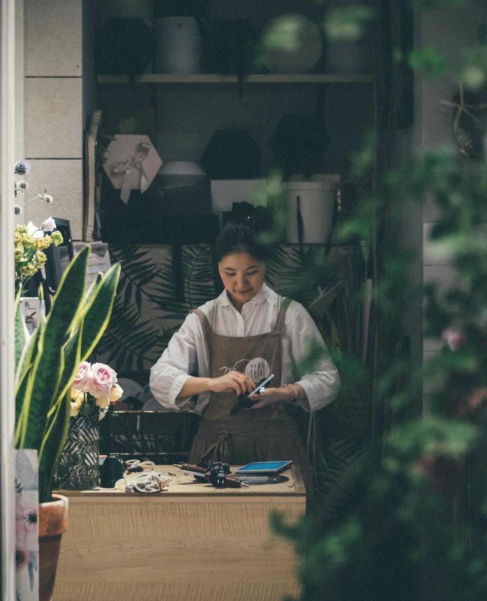 A florist at her shop counter, seen through the front window.